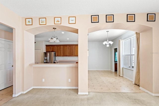 kitchen featuring light carpet, an inviting chandelier, hanging light fixtures, stainless steel fridge, and kitchen peninsula