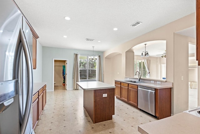 kitchen featuring sink, pendant lighting, a textured ceiling, a kitchen island, and appliances with stainless steel finishes