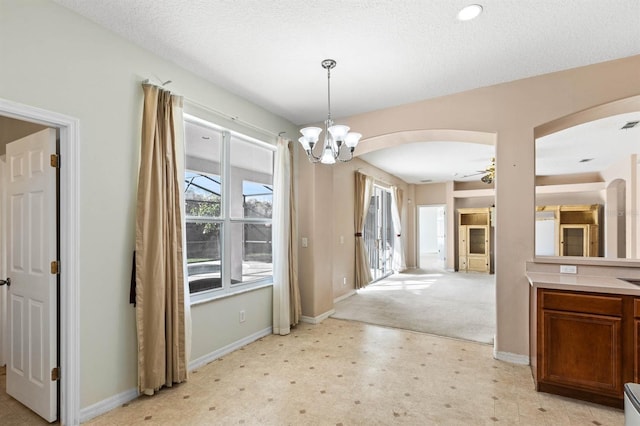 unfurnished dining area featuring a textured ceiling and ceiling fan with notable chandelier