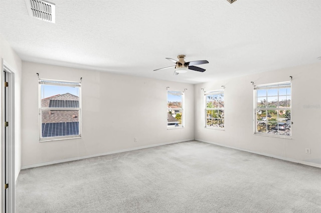 carpeted empty room with ceiling fan, a healthy amount of sunlight, and a textured ceiling