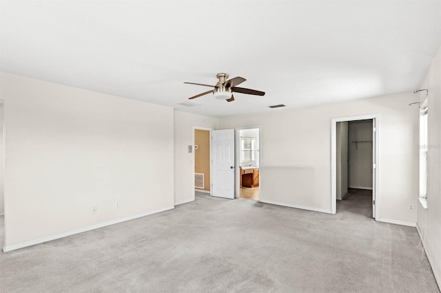 interior space featuring connected bathroom, ceiling fan, light colored carpet, a walk in closet, and a closet