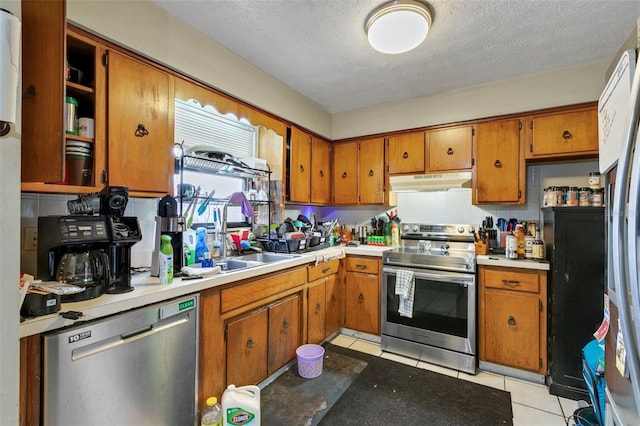 kitchen with appliances with stainless steel finishes, sink, light tile patterned flooring, a textured ceiling, and decorative backsplash