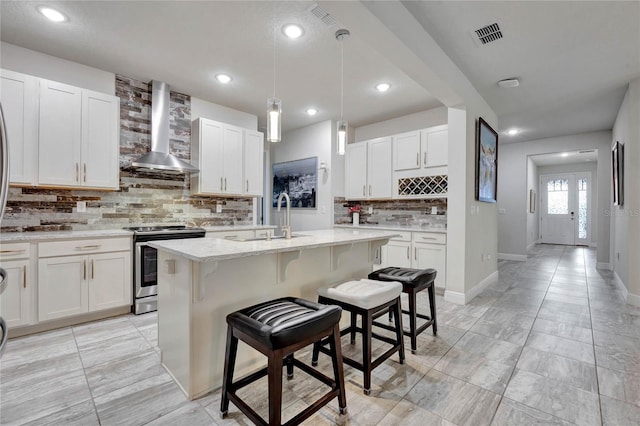 kitchen with a kitchen breakfast bar, light stone counters, wall chimney exhaust hood, a kitchen island with sink, and stainless steel range with electric cooktop