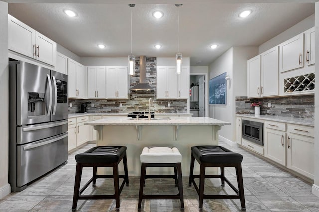 kitchen featuring built in microwave, wall chimney exhaust hood, stainless steel refrigerator with ice dispenser, a kitchen island with sink, and white cabinets