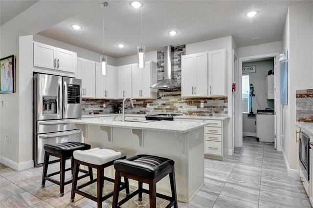 kitchen with a kitchen island with sink, white cabinets, wall chimney range hood, a kitchen bar, and stainless steel fridge with ice dispenser