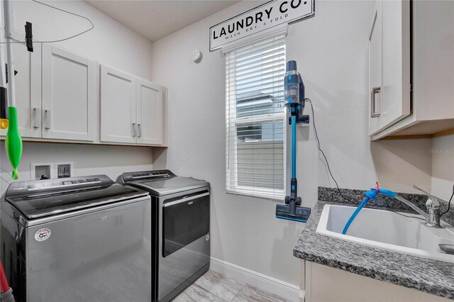 clothes washing area with separate washer and dryer, sink, and cabinets