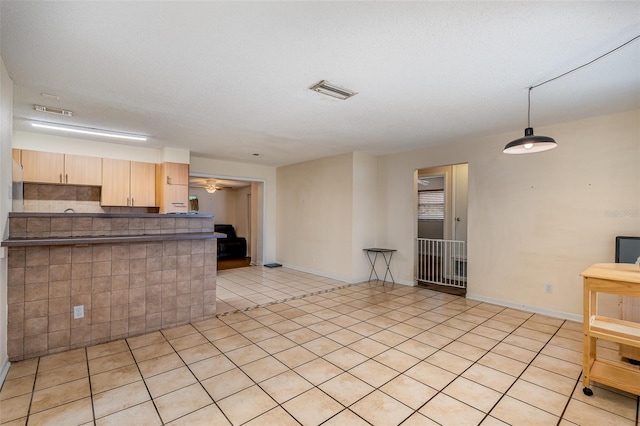 kitchen with kitchen peninsula, light brown cabinets, a textured ceiling, and light tile patterned floors