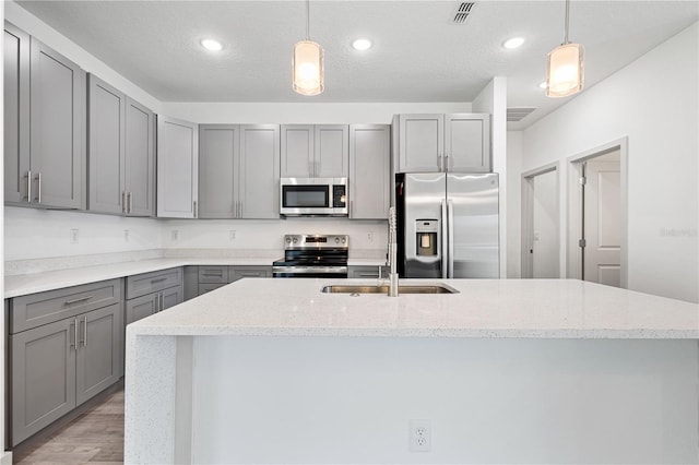 kitchen with gray cabinetry, light stone counters, hanging light fixtures, and appliances with stainless steel finishes