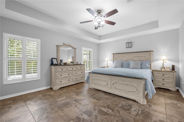 bedroom featuring ceiling fan, multiple windows, and a tray ceiling