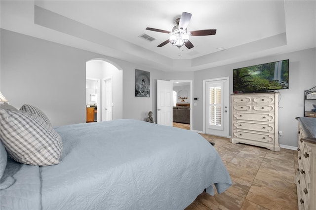 bedroom featuring a raised ceiling, ceiling fan, and ensuite bathroom