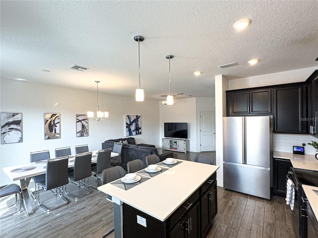 kitchen with pendant lighting, a kitchen island, an inviting chandelier, tasteful backsplash, and stainless steel refrigerator