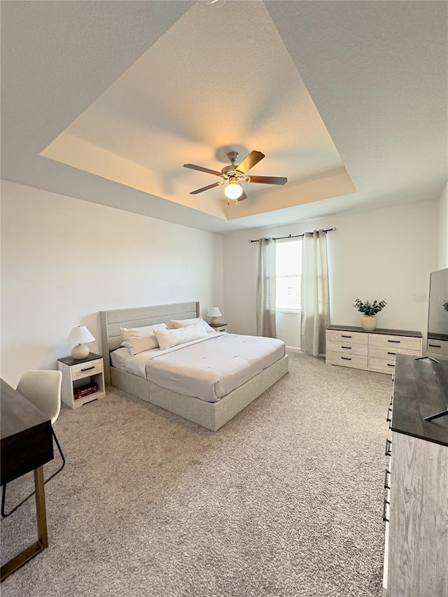 carpeted bedroom with ceiling fan and a raised ceiling