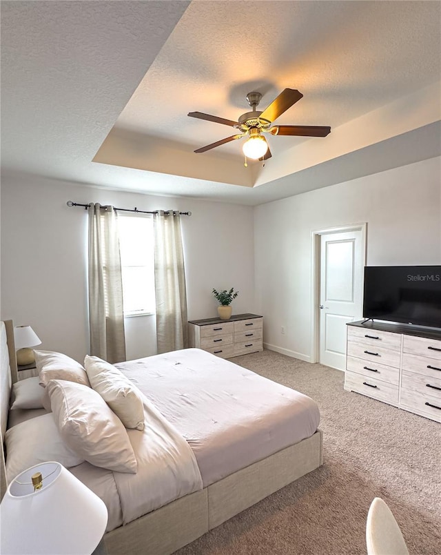 carpeted bedroom with ceiling fan, a tray ceiling, and a textured ceiling