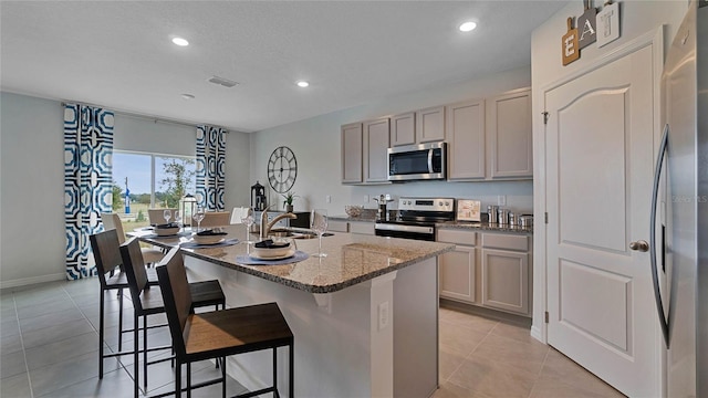 kitchen with light stone counters, stainless steel appliances, a kitchen island with sink, sink, and a breakfast bar area