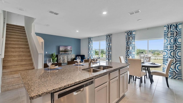 kitchen with light stone countertops, stainless steel dishwasher, sink, an island with sink, and light tile patterned flooring