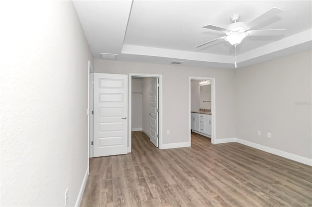 unfurnished bedroom with ensuite bathroom, a raised ceiling, ceiling fan, a spacious closet, and a closet