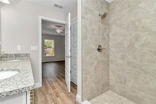 bathroom featuring a tile shower, ceiling fan, vanity, and wood-type flooring