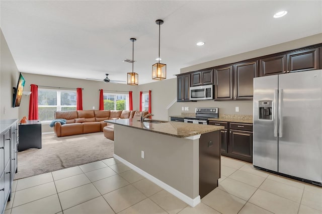 kitchen featuring a center island with sink, ceiling fan, light stone countertops, decorative light fixtures, and stainless steel appliances