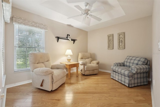 living area with ceiling fan, a raised ceiling, and light hardwood / wood-style flooring