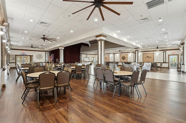 dining space with wood-type flooring, a drop ceiling, ornate columns, and ceiling fan