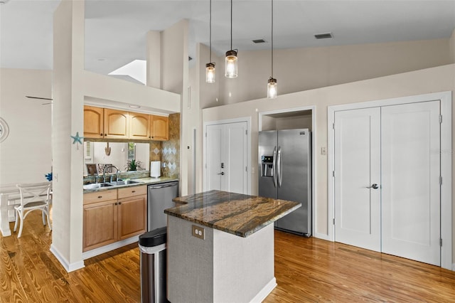 kitchen featuring lofted ceiling, dark stone counters, sink, hanging light fixtures, and stainless steel appliances