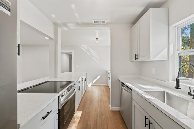 kitchen with sink, light stone countertops, light hardwood / wood-style floors, white cabinetry, and stainless steel appliances