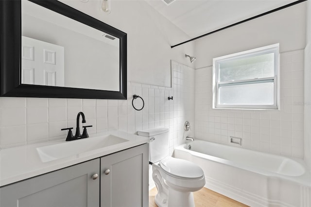 full bathroom with tiled shower / bath combo, toilet, decorative backsplash, vanity, and hardwood / wood-style flooring