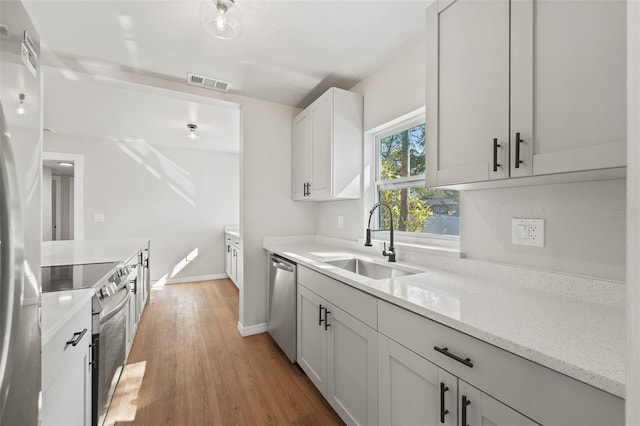 kitchen featuring sink, light stone countertops, appliances with stainless steel finishes, white cabinetry, and wood-type flooring