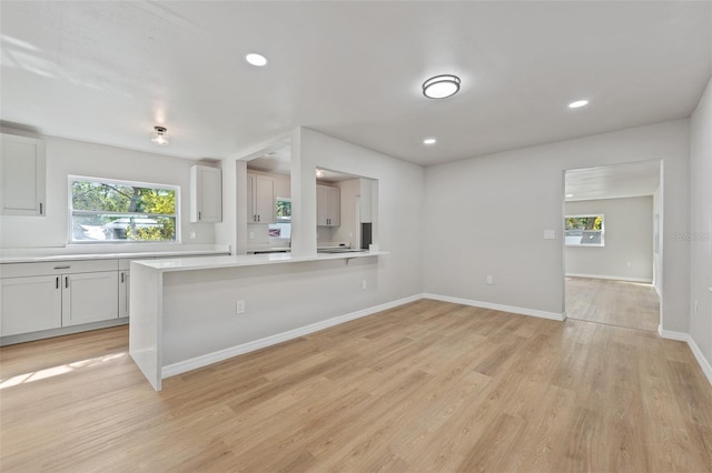 kitchen with a healthy amount of sunlight, light wood-type flooring, white cabinetry, and kitchen peninsula