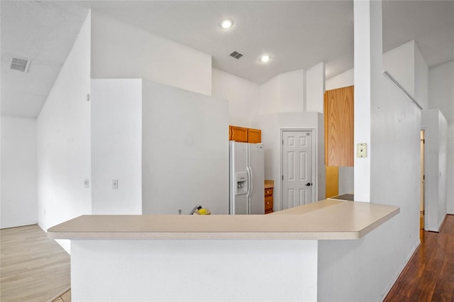 kitchen with kitchen peninsula, a towering ceiling, white fridge with ice dispenser, and hardwood / wood-style floors