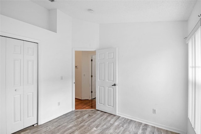 unfurnished bedroom with a textured ceiling, a closet, a towering ceiling, and light hardwood / wood-style flooring