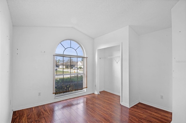 unfurnished bedroom featuring a textured ceiling, a closet, lofted ceiling, and dark hardwood / wood-style floors