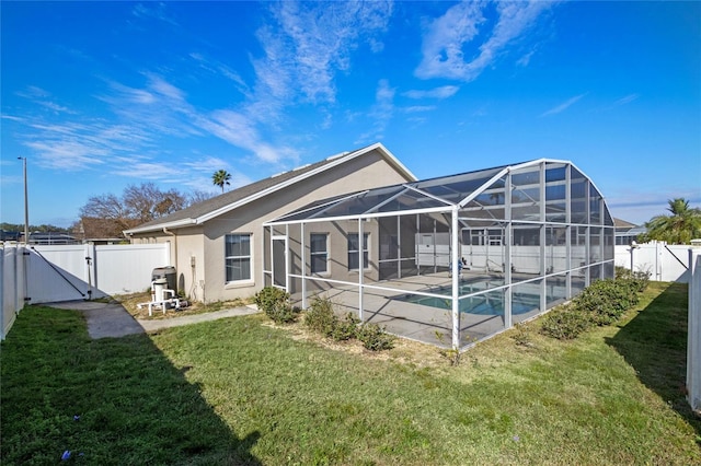 rear view of property featuring glass enclosure, a fenced in pool, a lawn, and a patio