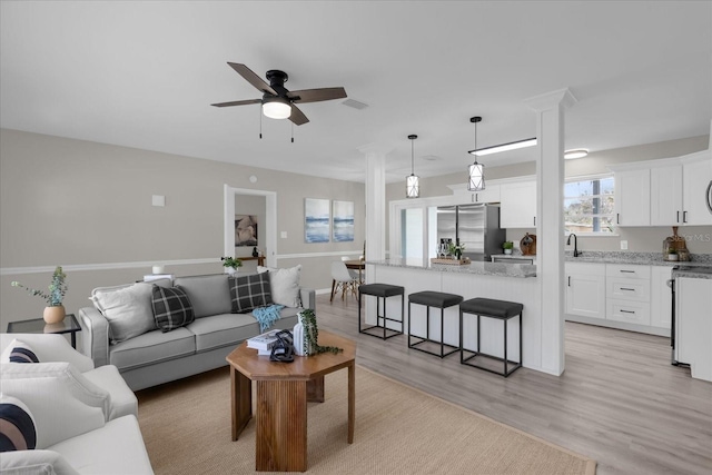 living room featuring light hardwood / wood-style floors, ornate columns, ceiling fan, and sink