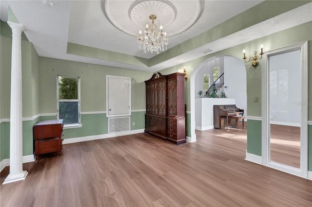 interior space featuring a raised ceiling, ornate columns, wood-type flooring, and an inviting chandelier