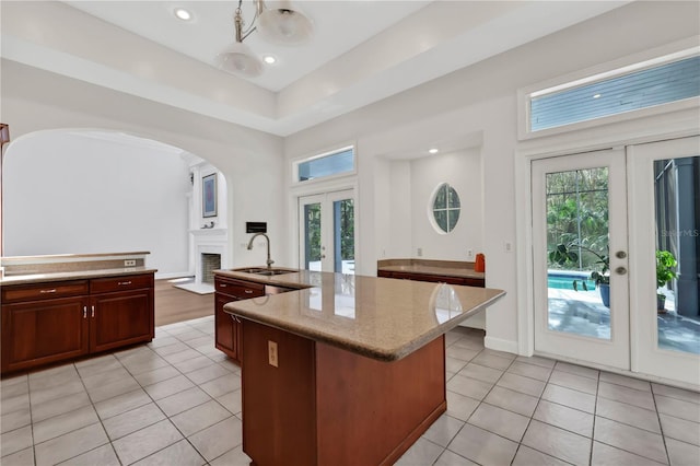 kitchen featuring french doors, a brick fireplace, sink, light tile patterned floors, and an island with sink