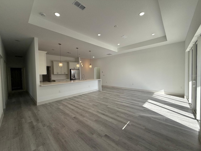 unfurnished living room with light hardwood / wood-style floors, a raised ceiling, and sink