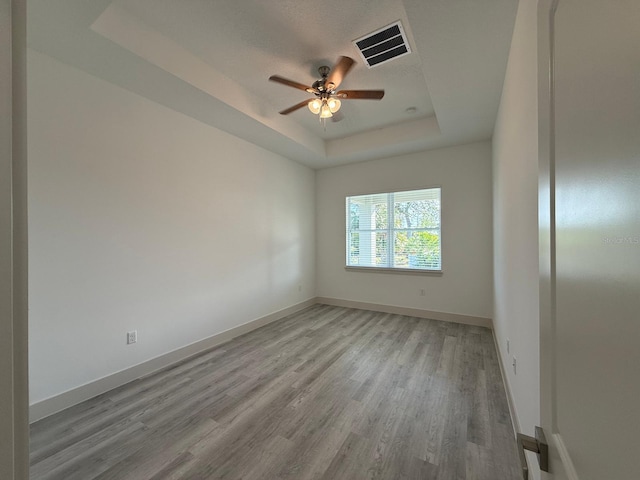 empty room featuring light hardwood / wood-style floors, a raised ceiling, and ceiling fan