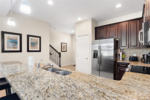 kitchen with light stone countertops, dark brown cabinetry, stainless steel appliances, sink, and hanging light fixtures