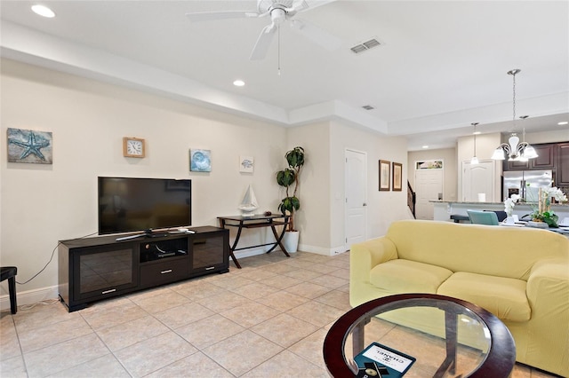 tiled living room featuring a tray ceiling and ceiling fan with notable chandelier