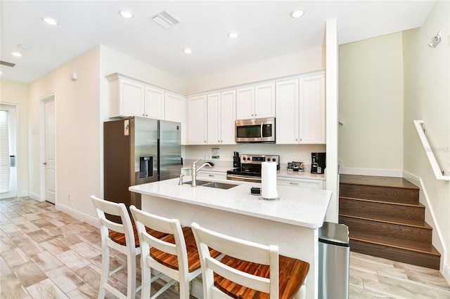 kitchen featuring light stone countertops, a center island with sink, white cabinets, and appliances with stainless steel finishes