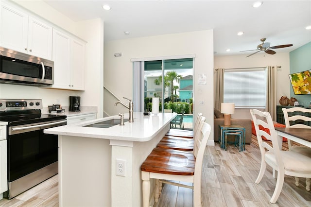 kitchen with a kitchen island with sink, sink, ceiling fan, appliances with stainless steel finishes, and white cabinetry