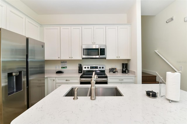 kitchen featuring light stone countertops, appliances with stainless steel finishes, white cabinetry, and sink