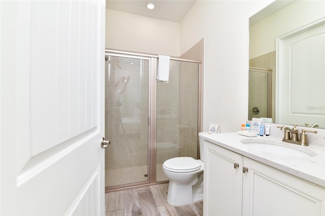 bathroom with hardwood / wood-style floors, vanity, toilet, and a shower with shower door