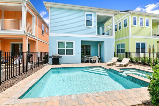 rear view of house featuring a balcony, a patio, and a pool with hot tub