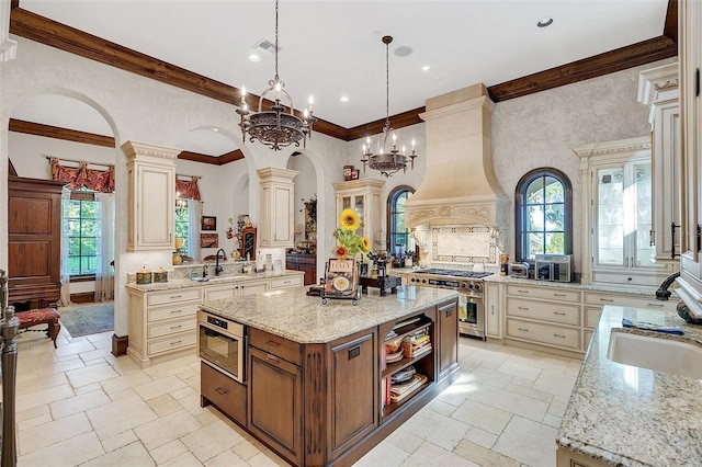 kitchen with decorative light fixtures, premium range hood, an island with sink, and cream cabinets