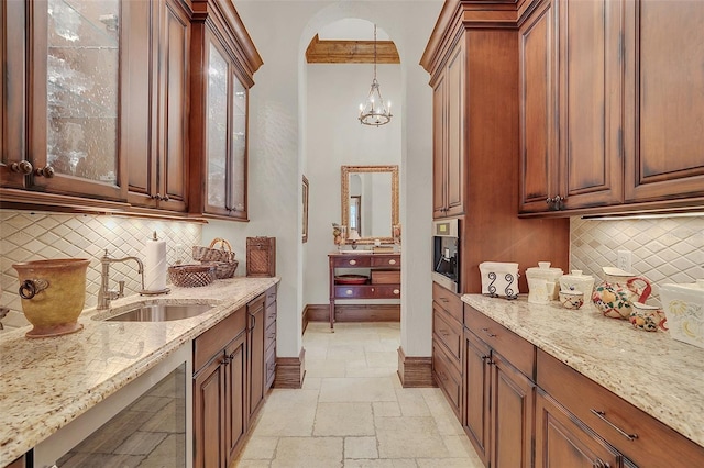 kitchen with light stone countertops, sink, hanging light fixtures, a notable chandelier, and decorative backsplash