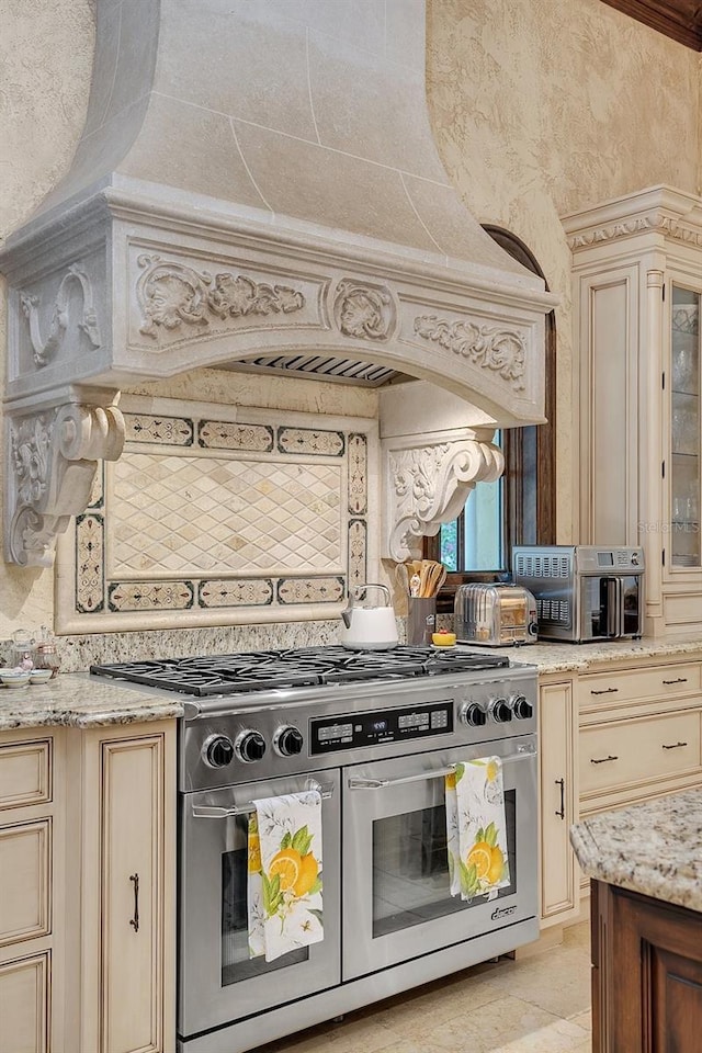 kitchen featuring cream cabinetry, decorative backsplash, range with two ovens, and ornamental molding