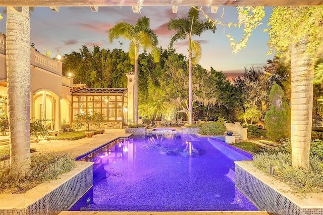 pool at dusk featuring a patio area and an in ground hot tub