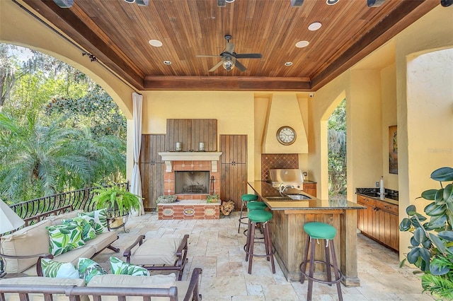 view of patio / terrace with an outdoor living space with a fireplace, ceiling fan, an outdoor wet bar, and exterior kitchen